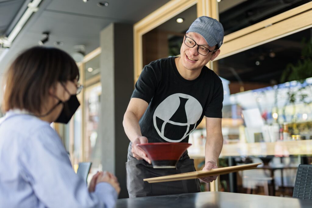 笑顔でうどんをお客様に運ぶ